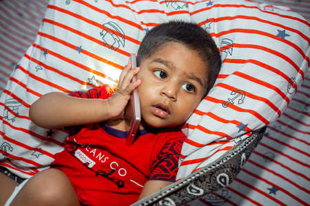 Before going to sleep a child is lying a homemade hammock and watching cartoons using a smartphone. Kids playing with smartphone. Mobile phone and internet addiction concept.の写真素材