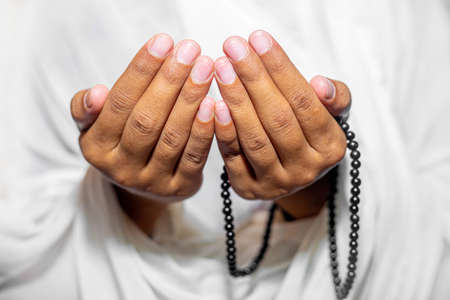 Muslim women raise their hands to pray with a Tasbeeh on white background, indoors. Focus on hands.の写真素材