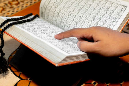 Muslim woman reading the Holy Quran using the finger. The Holy Quran on the mat of prayers ....