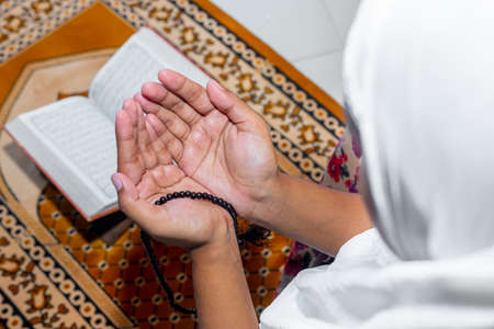 Muslim Asian women raise their hands to pray on the mat at home. Indoors. Focus on hands.