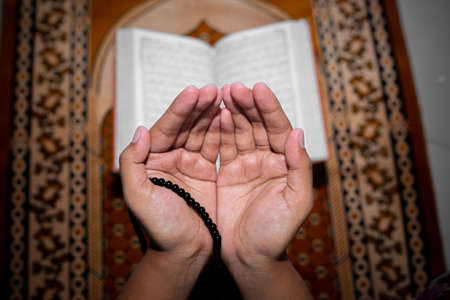 Young Muslim woman praying with Tasbeeh. The Holy Quran is the background, Indoors. Focus on hands.