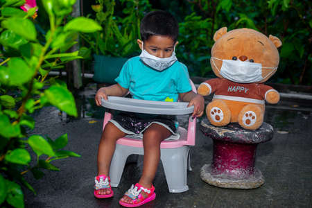 A child and his doll spend time sitting in the garden wearing face masks in on coronavirus pandemic time.の写真素材