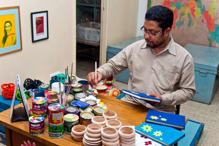 Bangladesh â€“ February 16, 2014: A handicraft artist is painting on a handmade book cover...