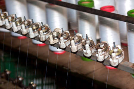 Red-green spools of white yarn in a garment factory. Weaving loom in a textile factory.の写真素材