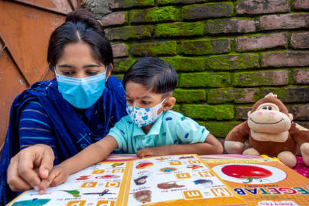 Bangladesh â August 02, 2021: In the lockdown and home quarantine of the Covid-19 epidemic, an Asian mother is teaching her child at home wearing a mask at Joypara, Dohar, Dhaka.のeditorial素材