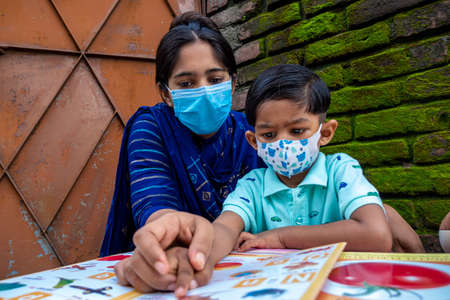 Bangladesh â August 02, 2021: In the lockdown and home quarantine of the Covid-19 epidemic, an Asian mother is teaching her child at home wearing a mask at Joypara, Dohar, Dhaka.のeditorial素材