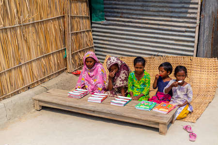 Bangladesh â€“ March 06, 2021: A lady teacher is sitting on the outdoor in front of a house in...