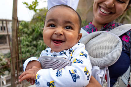 A mother is having fun with her cute baby boy in a portable carry bag. Expressing warm loving caring...