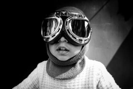 A toddler boy's discovery, adventure, and curious face. Close-up view of a kid boy dressed as a pilot. Black and white vintage photograph.の写真素材