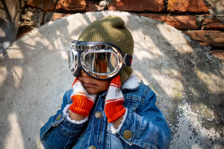 A pilot boy is wearing an old blue jeans jacket and hand gloves on a heavy winter day. A happy kid...