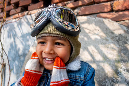 A pilot boy is wearing an old blue jeans jacket and hand gloves on a heavy winter day. A happy kid...