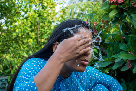A woman splashes cold water on her face on a hot day. Closeup view of a young girl cleaning her face with water. Happy beautiful girl washes her face with pure water.の写真素材