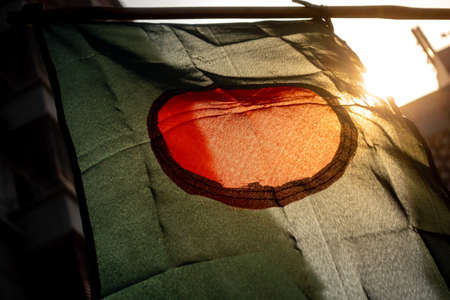 The national flag of Bangladesh is flying in the sky. The flag of Bangladesh is made of a center red circle in green. Close Up View of the national flag of Bangladesh made of Silk fabric.の写真素材