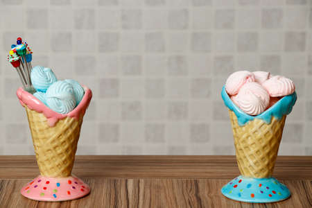 blue and pink meringue in the pink and blue cones with cupcakes on wood table white background