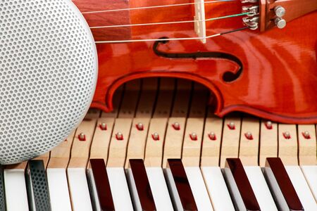 modern speaker and classical violin on white and black piano keys close-up background