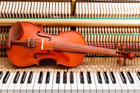 classic brown violin on the close up image of grand piano keys and interior showing strings, hammer and structure backgroundの写真素材