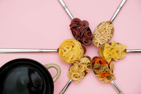 Raw colored tagliatelle, spaghetti and pasta on metal spoons, black pot on pink flat ray backgroundsの写真素材