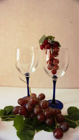 A bunch of red grapes along with 2 wine glasses  for celebration event.