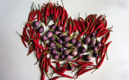 Red hot peppers have a very spicy flavor in a heart image with eggplants put on white background.