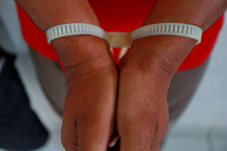 Man handcuffed hands. Prisoner or arrested. close-up of hands in handcuffs, selective focus. Close Up image of a Handcuffed Convict at a Law and Justice Court Trial. Handcuffs on Accused Criminal in Jail Jumpsuit.の写真素材