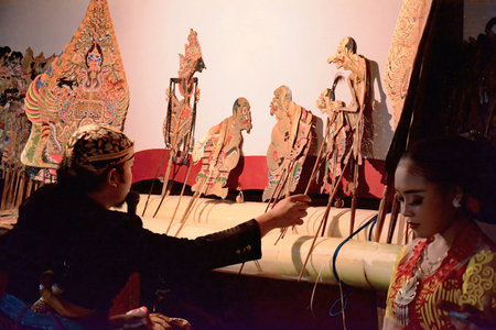 Traditional Javanese shadow puppet show featuring a dalang, colorful wayang kulit puppets, and gamelan musicians in cultural performance setting.の素材