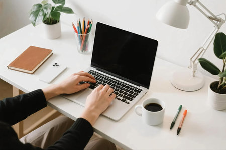 Modern minimalist workspace with laptop, coffee, notebook, smartphone, lamp, pens, and plant on white desk. Perfect for concepts of remote work, freelance, productivity, creativity, and home office.の素材