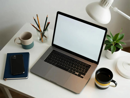 Minimalist desk setup with laptop, smartphone on notebook, coffee cup, potted plant, pencils in glass, and lamp. Perfect for themes of remote work, productivity, freelance lifestyle, and creativity.の素材