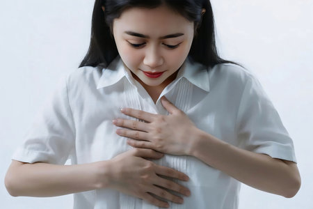 Young woman experiencing stomach pain while standing in a studio with a concerned expression, showcasing discomfort and health issues.の素材