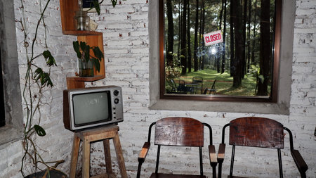 Retro television sits on wooden stool inside rustic cafe with forest view through window, creating nostalgic and cozy atmosphere.の写真素材