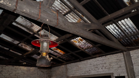 Old lantern hangs from weathered wooden beams in abandoned barn, casting dim light on decaying interior with rustic charm and forgotten history.の写真素材