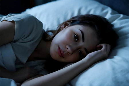 Pensive woman lies in bed at night, illuminated by moonlight, contemplating her thoughts with a serene and melancholic mood.の素材