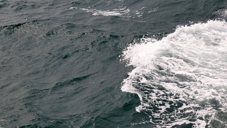 Ocean wave crashes on the surface of the deep blue sea, creating white foam and a sense of power and...