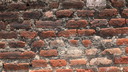 Old brick wall shows signs of age and weathering with crumbling mortar and faded red bricks,...