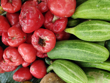 Rose apples pile, cucumber on banana leaf at outdoor market, offering a vibrant and tropical display of fresh produce in a bustling atmosphere.の写真素材
