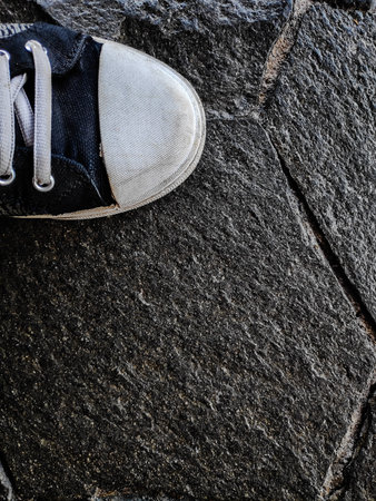 Sneaker steps onto dark gray stone pavement creating a textured contrast in urban setting, showcasing a casual and modern lifestyle.の写真素材
