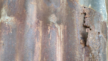 Corrugated metal sheet displays rust and corrosion in an industrial setting, showing the effects of...