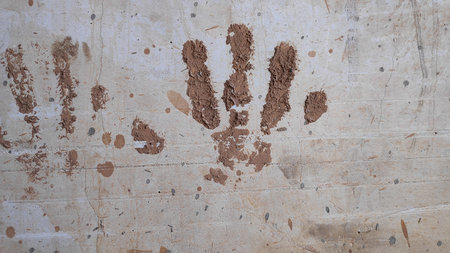Mud splatters cover a weathered concrete wall, creating an abstract pattern with earthy tones and...