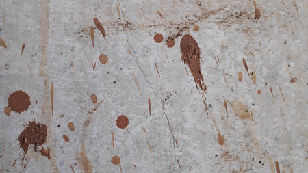 Abstract textured surface displays stains and splatters of brown paint on a light gray backdrop,...