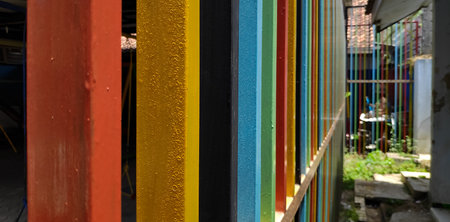 Colorful metal beams stand together creating a vibrant fence in an outdoor space, showcasing a playful and modern aesthetic with a sense of unity and creativity.の写真素材