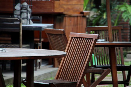 Wooden chairs and tables sit peacefully on a patio surrounded by lush greenery, creating a relaxing...
