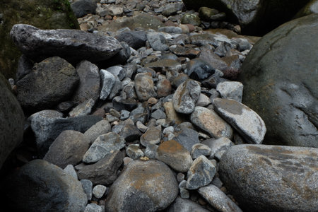 Pile of smooth rocks and pebbles fills riverbed in a natural environment, showcasing texture and geological formations in a peaceful scene.の写真素材