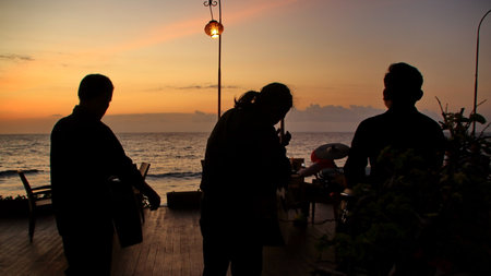 Three musicians play steel drums on a wooden pier at sunset, creating a peaceful and relaxing atmosphere with the ocean waves in the distance.の写真素材