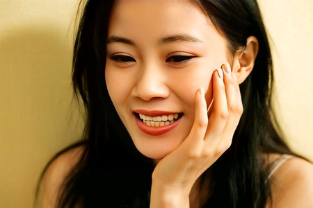 Pensive young woman gently touches her cheek indoors, lost in thought with soft, natural light creating a serene and contemplative atmosphere.の素材