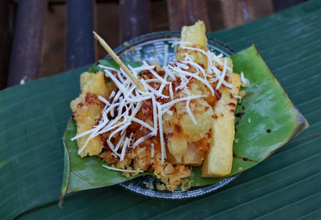 Fried cassava topped with shredded cheese served on banana leaf at street food vendor stall in Southeast Asia, a delicious and tempting snack.の写真素材