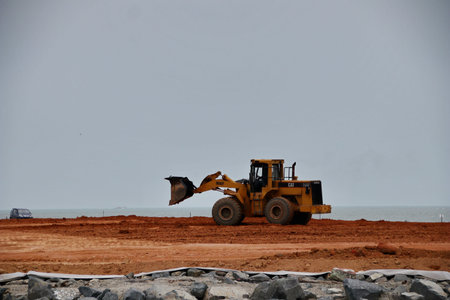 A yellow tractor working on a sandy field near the beach under the open sky