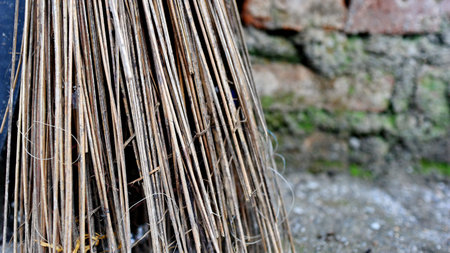 Close up traditional broom made of natural twigs leans against an old red brick wall, showing rough textures, earthy tones, and a quiet rustic atmosphereの写真素材