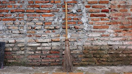 A simple broom stands quietly against a weathered brick wall, highlighting natural materials, aged surfaces, and a calm rural atmosphere filled with subtle character.の写真素材