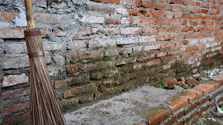 A weathered broom leans against an old brick wall, combining natural fibers and rough masonry to create a timeless rural scene filled with texture and character.の写真素材