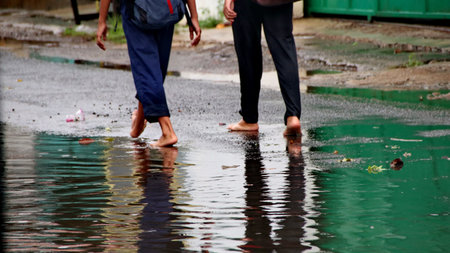 Reflection. Two teenage boys without shoes or footwear, walking on a road that is wet due to rain so that it pools and floods.の写真素材