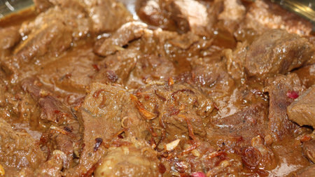 Close-up of a delicious, savory meat stew or curry, slow-cooked in a rich brown gravy. Garnished...
